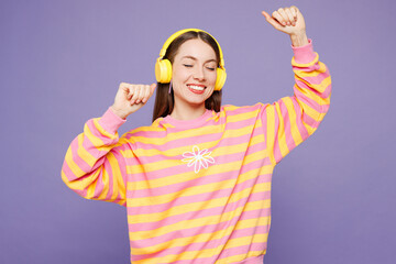 Young cheerful woman she wears yellow sweatshirt casual clothes listen to music in headphones raise...