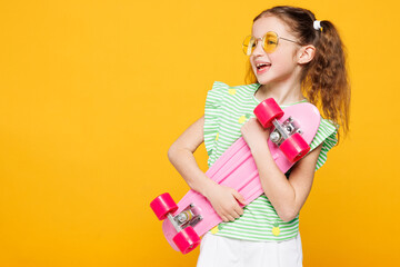 Little cute kid child girl 8-9 years old wears green t-shirt sunglasses hold in hand skateboard...