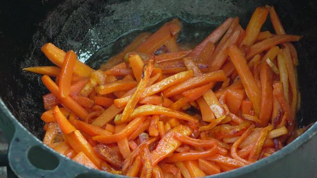 Carrots frying cooking, delicious vegetables sizzle in a large pot, preparing food outdoors
