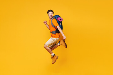 Young winner traveler man carry backpack with stuff mat jump high isolated on plain yellow...