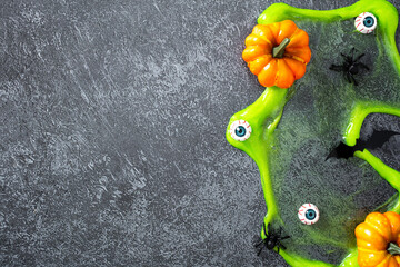 Spooky Halloween flat lay with green slime, eyeballs, pumpkins, spiders, and bat silhouette on...