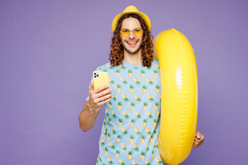 Young smiling fun man wear blue beach t-shirt yellow hat sunglasses rest near hotel pool hold...