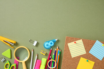 Colorful school and office supplies on green background, including pencils, magnifying glass, and...