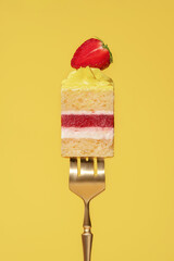 Colorful lemon and strawberry bento cake slice with layers of cream, fruit, and sponge on a golden fork against a vibrant yellow background, showcasing a delightful dessert concept