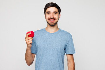 Young smiling happy man wear blue t-shirt casual clothes hold in hand eat bite red apple look...