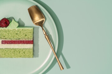 Colorful bento cake slice with layers of green pistachio, cream, and raspberry filling, elegantly presented on a pastel plate with a golden serving utensil, showcasing a delightful dessert concept
