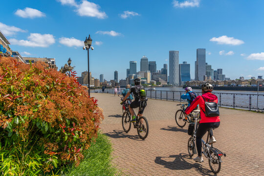 View of cyclists on the Thames Path at Wapping and Canary Wharf Financial District in the background, London, England