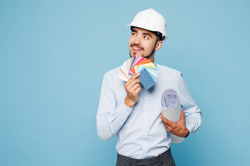 Young architect engineer designer employee man wears white clothes shirt hardhat hold blueprints color palette look aside isolated on plain light blue background studio portrait Work on build project