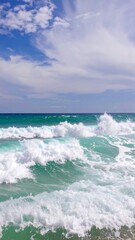 Fototapeta premium Turquoise waves crashing on a beach, with a partly cloudy sky