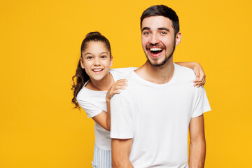 Fototapeta premium Young smiling parent man have fun with child girl in casual blue pyjamas clothes. Daddy little kid daughter posing looking camera isolated on plain yellow background. Father's Day Love family concept.