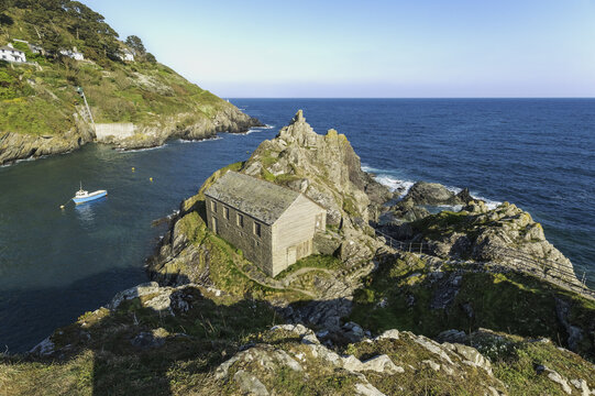 Looe, United Kingdom - 04 October 2025: View of a stone building perched atop rugged rocks, embraced by the turquoise sea and framed by verdant cliffs.