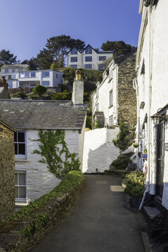 Looe, United Kingdom - 04 October 2025: View of white-washed cottages nestled on a hillside, a glimpse of blue sky peeking above, a serene coastal charm captured in time.