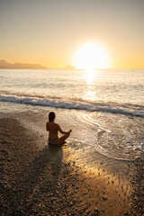 Fototapeta premium Young woman meditating on beach at sunrise, serene atmosphere