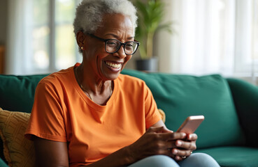 Smiling senior woman wearing glasses, sitting on green couch, using smartphone. Actively engaged with device, possibly browsing texting. Image reflects modern lifestyle for retired individuals,