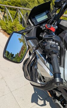 Vista de cerca de un protector de manos en manillar de motocicleta con reflejo de plantas en espejo retrovisor
