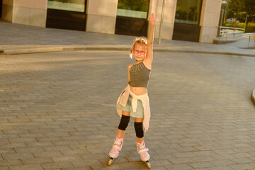 Smiling young girl with pink glasses roller skating outdoors at sunset, wearing casual black top and tied-around denim shorts, radiating childhood joy and energetic urban lifestyle