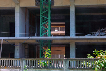 View into the interior of a multi-story concrete building under construction, showing support beams, debris, and a green crane tower.