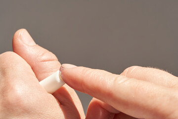 Adult caucasian hand applying moisturizing lip balm on finger with neutral background.