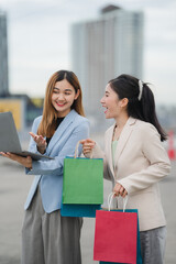 Shopping and Laptop Interaction: Two sophisticated women, surrounded by the urban landscape, share...