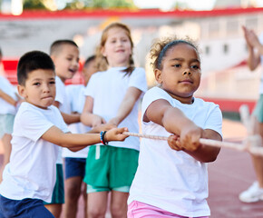 Children pulling a rope at the stadium, practice during sports class in school training, little fit boys and girls in sportswear training as athletes outdoor. Concept of sport, fitness and achievement