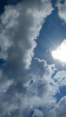 Bright sun and lens flare behind large white cumulus clouds in a blue sky

