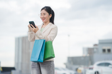 Shopping Delight: A stylish woman, clutching vibrant shopping bags, engages with her smartphone,...