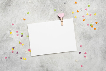 Blank card mockup with heart-shaped clip on gray background, surrounded by colorful confetti...