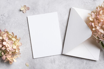 Blank wedding invitation card mockup with envelope, surrounded by delicate pink hydrangea flowers, top view with copy space