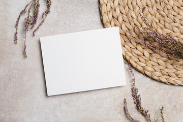 Blank white card mock up placed on a textured surface with woven mat and dried flowers, creating a serene and inviting atmosphere for design purposes