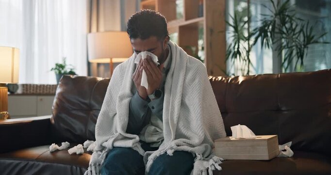 Man, blowing nose and tissue on sofa with flu, infection and blanket for recovery in living room. Person, sick and fatigue on couch with virus, mucus or cold with rest, healing or exhausted at home