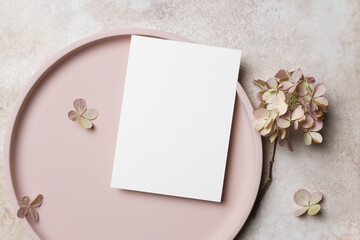 Blank white card mockup on a round pink plate surrounded by dried flowers, creating a serene and elegant atmosphere perfect for invitations or greeting cards with copy space