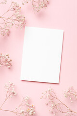 Blank white wedding invitation card mockup surrounded by delicate flowers on soft pink background, creating an elegant and inviting atmosphere for design and creative projects