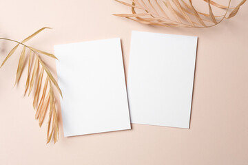 Blank white sheets of paper positioned on a soft pastel background with dried palm leaves, double cards for invitation or greeting cards design