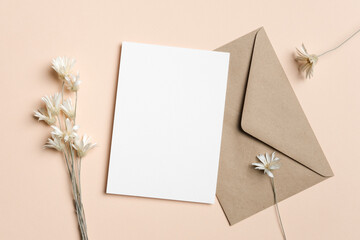 Blank white invitation or greeting card mockup with brown envelope and dried flowers, copy space for card designs presentation