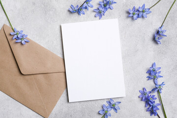 Blank white paper invitation or greeting card with brown envelope and delicate blue flowers on a textured gray surface, creating a serene and inviting atmosphere for personal messages