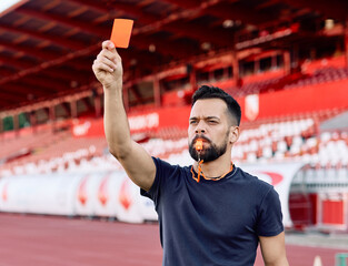 Portrait of a  soccer referee blowing a whistle and showing a yellow red card on stadium soccer field © Lumos sp