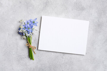 Bouquet of delicate blue and white flowers tied with twine, placed beside a blank card with copy space on textured gray surface, perfect for greeting or invitation design
