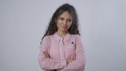 South Asian woman with curly hair, in a pink shirt, stands with arms crossed, smiling slightly - Powered by Adobe