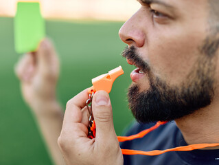 Portrait of a  soccer referee blowing a whistle and showing a yellow red card on stadium soccer...