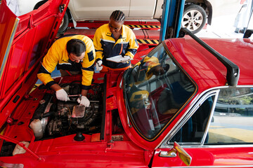 Diverse auto repair professionals work together under the hood of a red car in a modern garage....