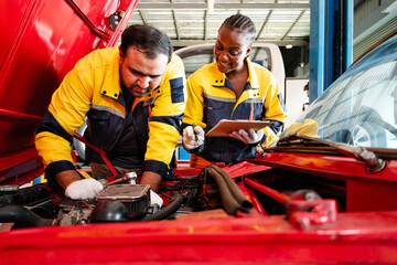 Diverse professional auto repair team working together on a car engine in a garage. Highlights...