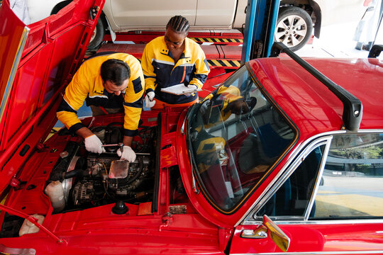 Diverse auto repair professionals work together under the hood of a red car in a modern garage. Showcasing teamwork, technical skill, and inclusive service in a trusted automotive workshop.