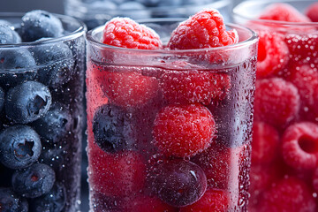 Red and blue frosted berries in glass exhibit water droplets, creating a refreshing drink product display.
