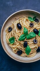 Top-down rustic bowl of spaghetti with black olives and basil