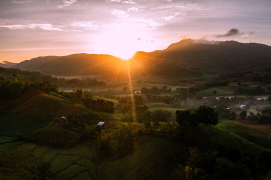 Aerial view of sunbeams pierce through the peaks, casting a golden glow over the verdant rice terraces and misty valleys of San Enrique, Iloilo, Western Visayas, Philippines.