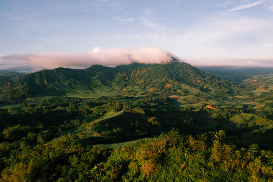 Aerial view of a verdant mountain shrouded in a blanket of low-hanging clouds, the landscape unfolds in shades of emerald and jade, San Enrique, Western Visayas, Philippines.