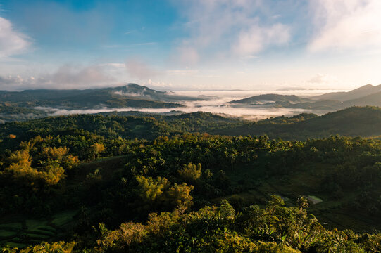 Aerial view of verdant hills rolling into the horizon, kissed by soft clouds and bathed in golden sunlight, San Enrique, Western Visayas, Philippines.