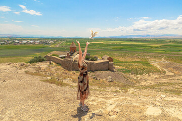 Blonde woman in long dress releasing a white dove with outstretched arms, set against the Khor...