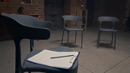 Close-up of clipboard with blank sheets for notes on chair of prison psychologist, prepared for group counseling or therapy meeting in hall of correctional facility