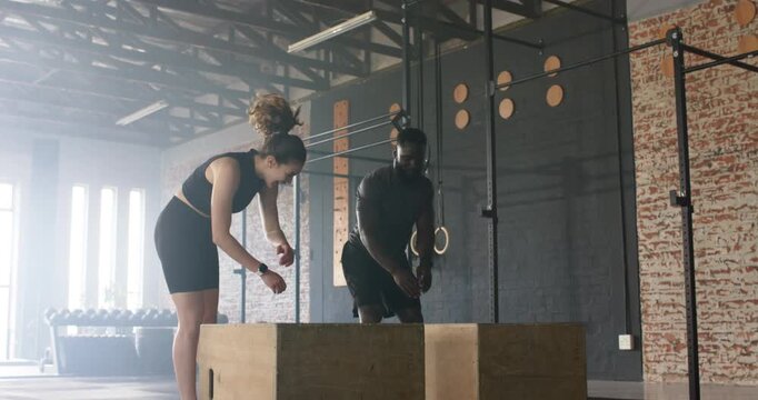 While squatting trainer and trainee performing rope-assisted, bodyweight box jumps in gym